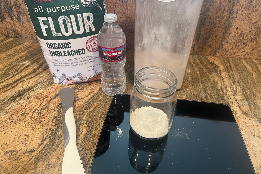 Sourdough starter ingredients including organic all-purpose flour, white whole wheat flour, water, a glass mason jar, kitchen scale, and spatula 